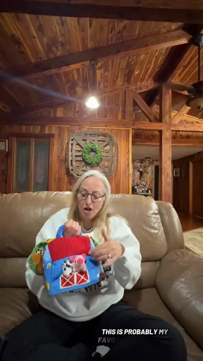 A person unfolds the same blue and red Farm barn and holds its plush cow